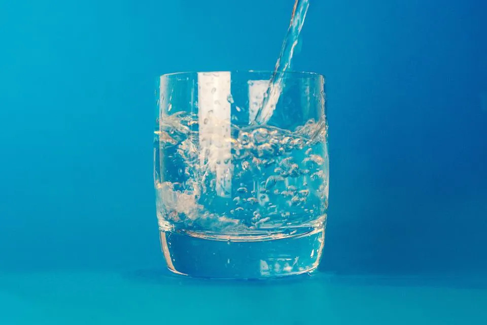 Clear glass being filled with water against a blue background