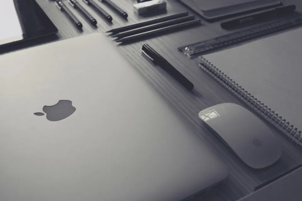 Laptop, notebook and pens neatly arranged on a dark desk
