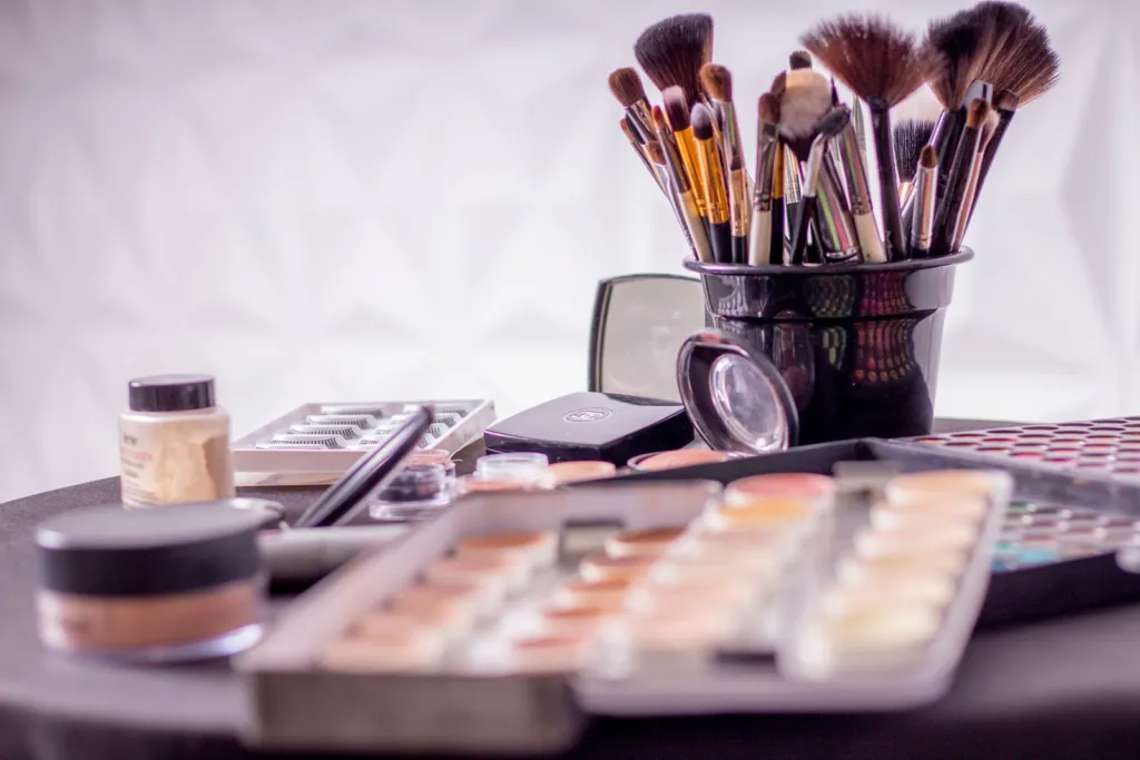 Makeup brushes standing in a black holder beside a palette and cosmetics