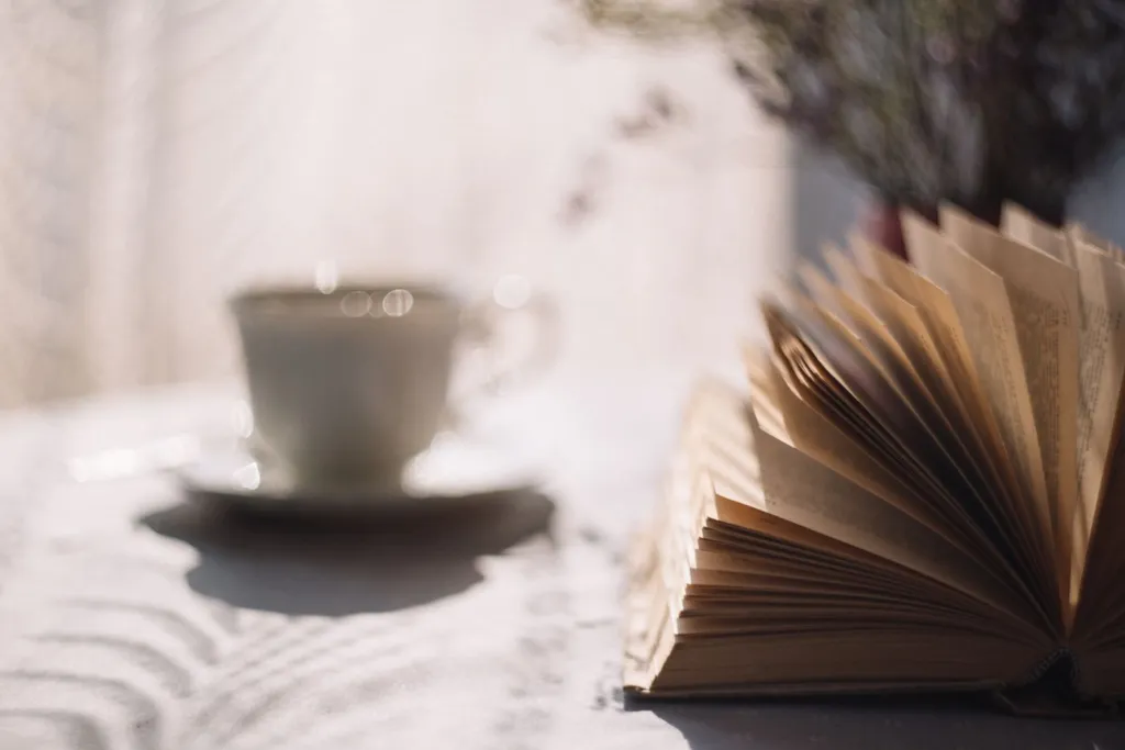 Open book on a sunlit table with a cup of coffee in the background