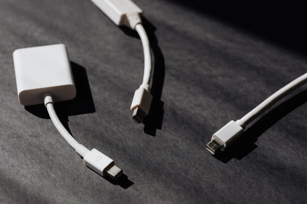 White charging cables and a display adapter lying on a dark desk