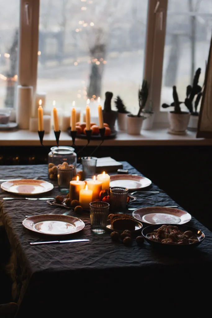 Dinner table set with plates, glasses and lit candles beside a window