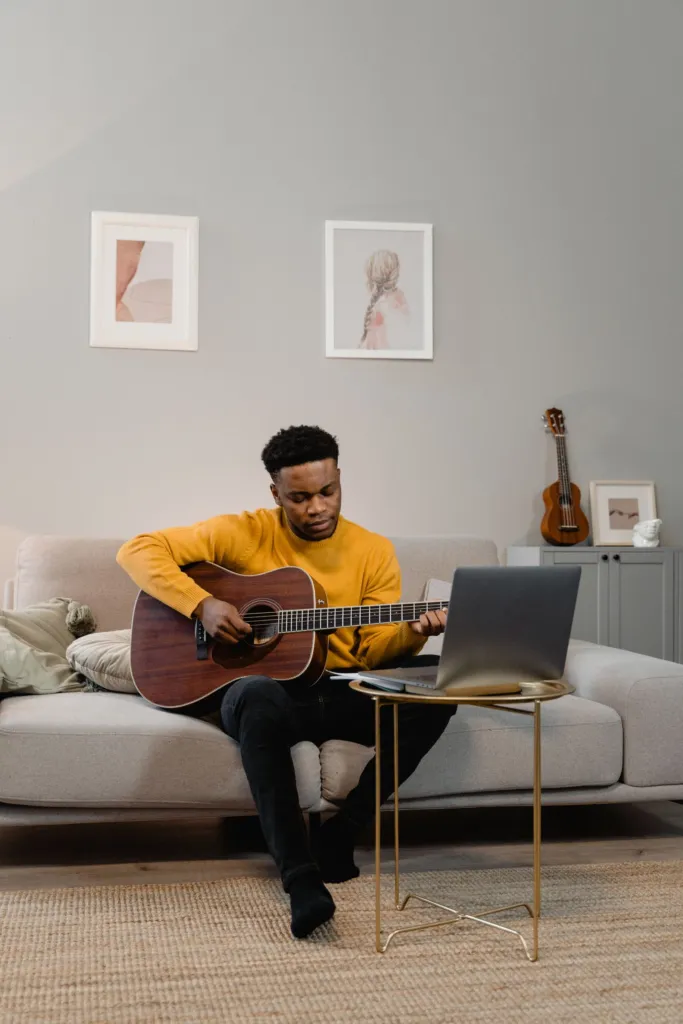Person sitting on a sofa at home practising an acoustic guitar