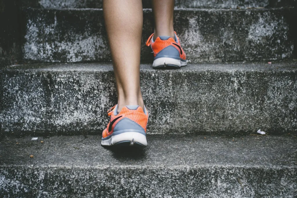 Close-up of a walker's feet in orange trainers stepping up outdoor stone stairs