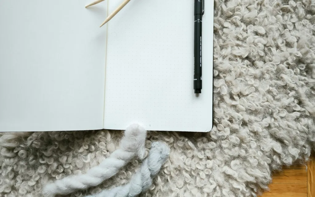 Open blank notebook with a black pen resting on a soft woven rug