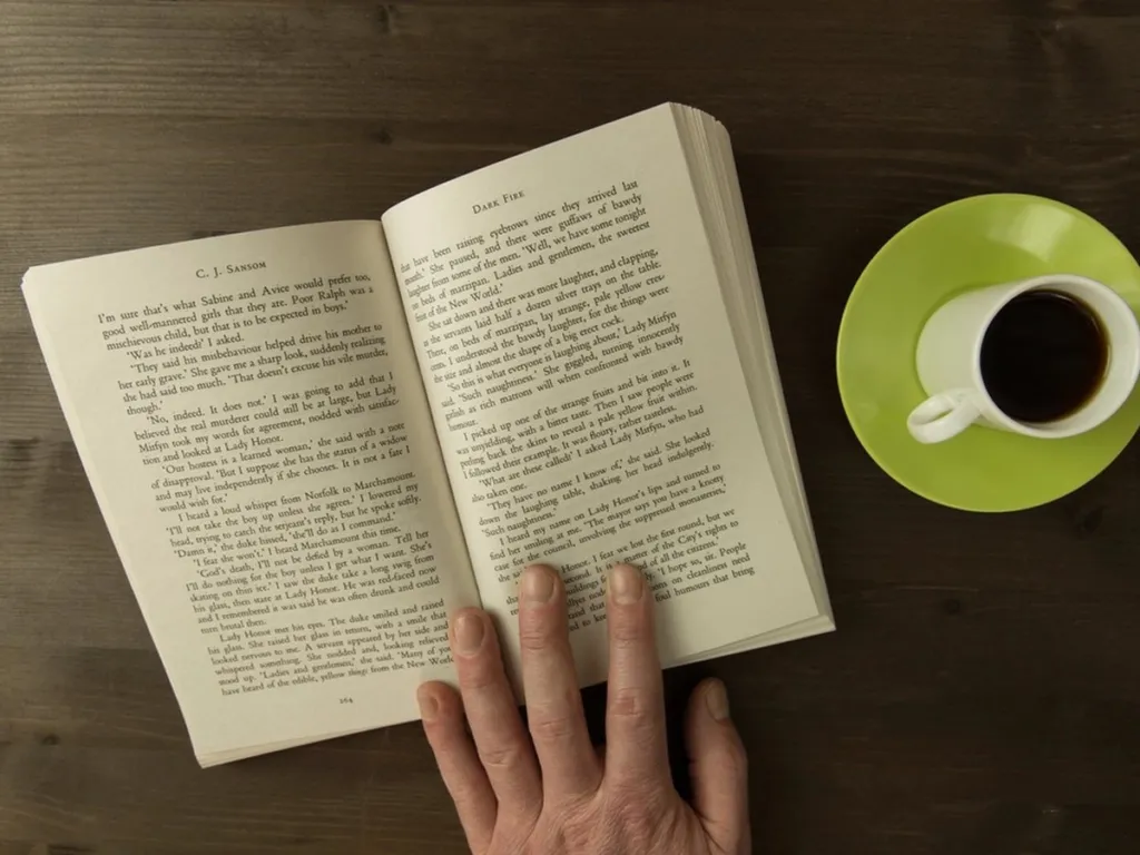 Open book beside a cup of coffee on a wooden table