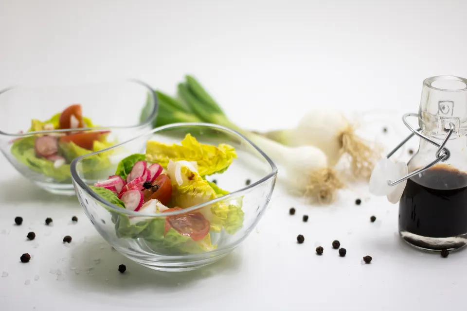 Glass bowls of fresh salad with spring onions and black pepper on a white table