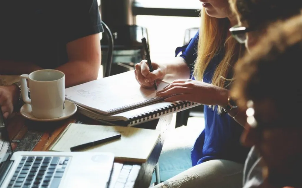 Team writing a simple business plan in notebooks around a table