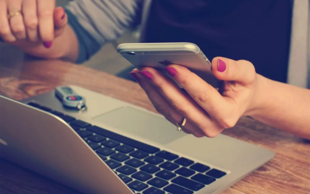 Person using a smartphone next to a laptop while signing in